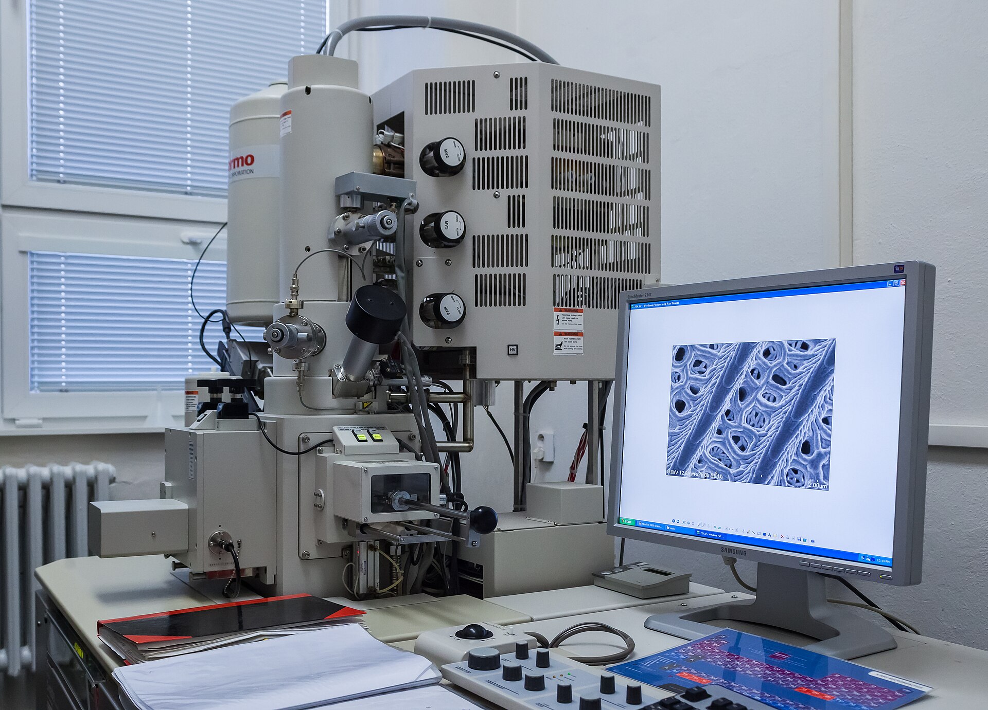 Microscope électronique à balayage et sa console dans une salle d'instrument ; une micrographie est affichée à l'écran.